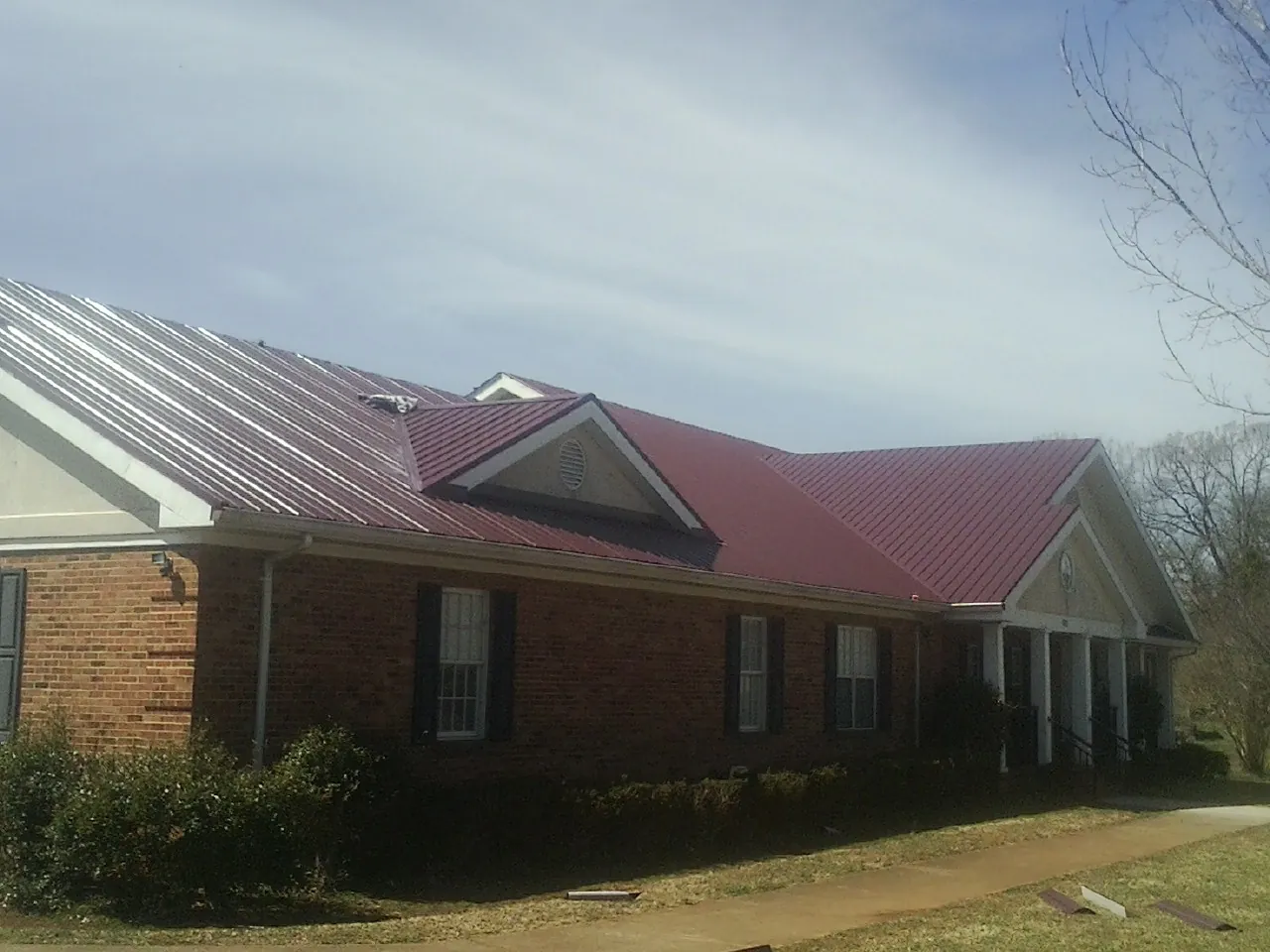 Red metal roof with gabled entries on a long brick building, from a Hail Damage Roof Repair job in Stinson Beach