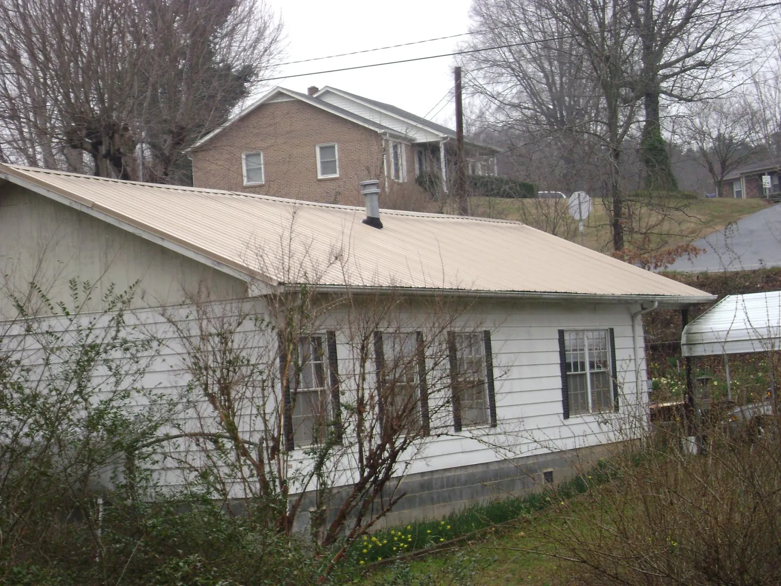Tan metal roof on a white sided house set into a hillside — Commercial Roofing by Roofing Brothers in Stinson Beach